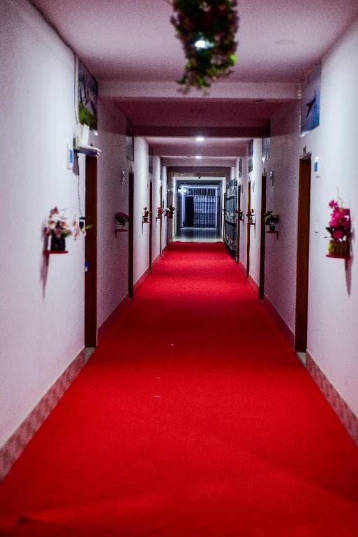 Interior hallway at Al Hera Resort with a red carpet runner, room doors on both sides, and small wall-mounted flower displays