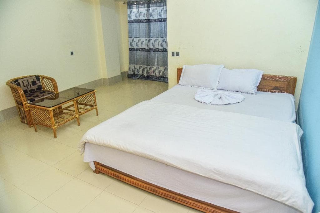 Cream-walled double bedroom at Al Hera Resort with a rattan armchair and glass coffee table beside a patterned curtain