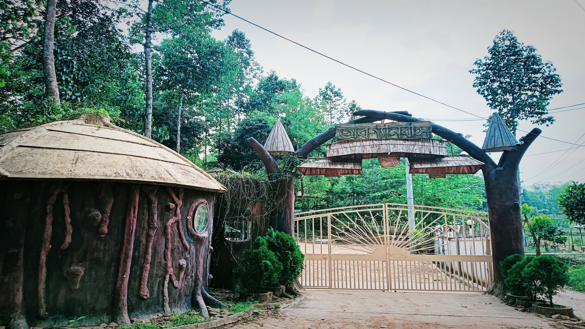 The whimsical tree-trunk entrance gate at Arannyo Nibas Eco Resort with the resort's name carved in Bangla overhead