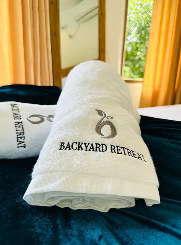 White towels embroidered with the Backyard Retreat logo, folded on a teal bedspread