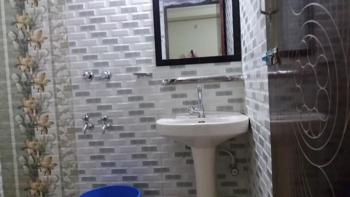 En-suite bathroom with white and grey subway-tile walls, a pedestal sink, wall-mounted mirror, and separate shower and bucket taps
