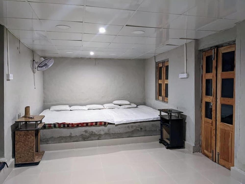 Guest room with a raised concrete sleeping platform, white bedding, wooden doors and a wall-mounted fan