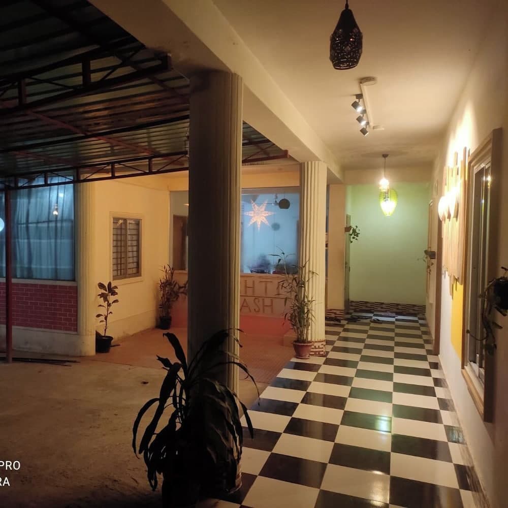 Night view of the covered corridor leading to reception, black-and-white checkered tile floor, potted plants, and partial 'BILASH' signage visible on the reception glass