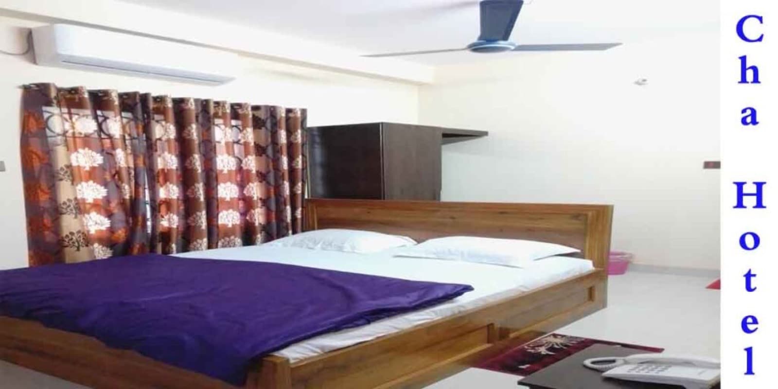A guest room at Cha Luxury Hotel with a wooden bed, patterned curtains and air conditioning