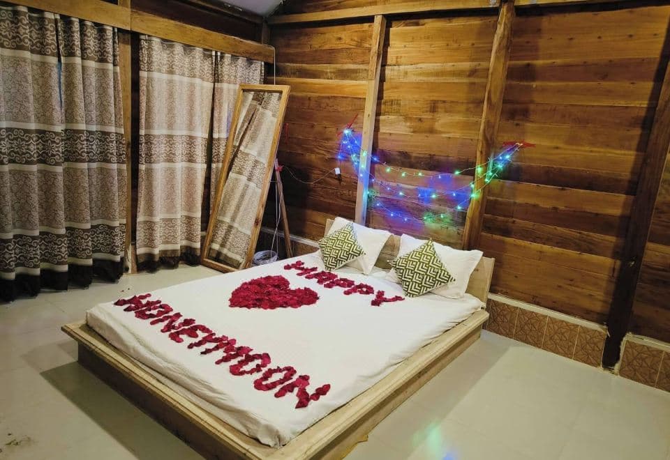 A wood-panelled honeymoon cottage room at Dolubari Eco Resort with a rose-petal bed display and string lights