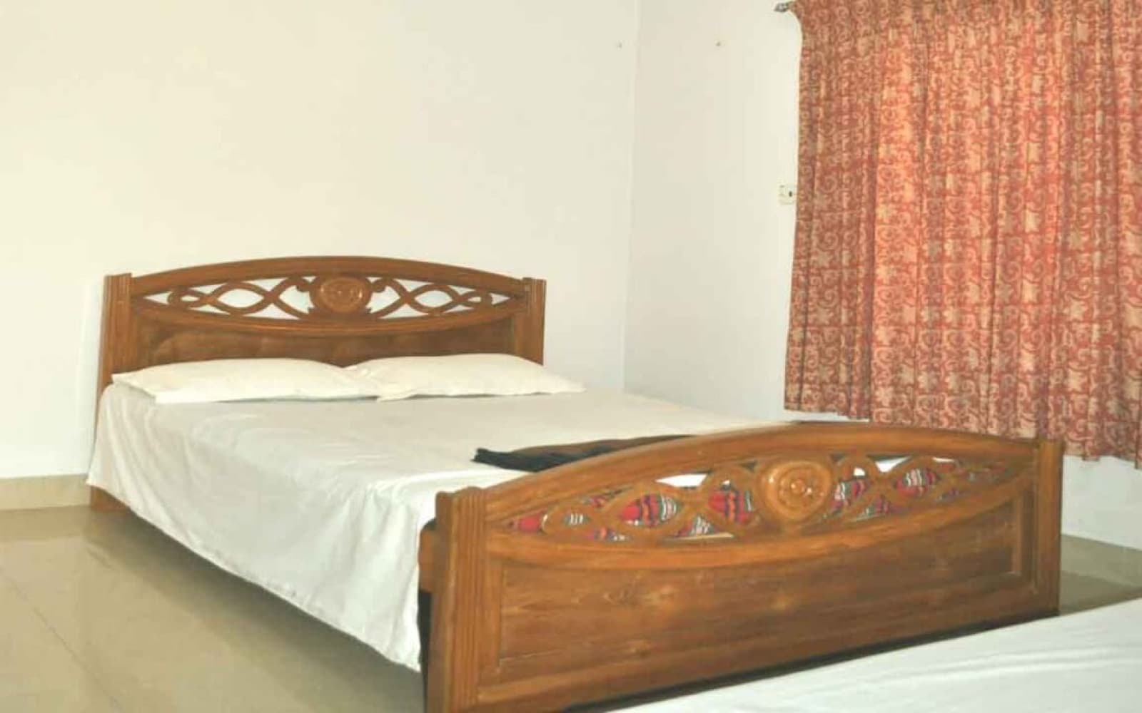 A double bed with a carved wooden headboard in a room at Garden View Guest House, Sreemangal