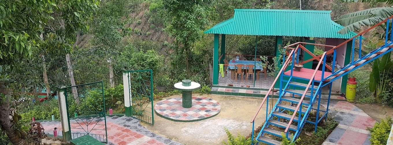Green Palace Tea Resort grounds with a tiled patio, green entrance gate, dining gazebo, and blue outdoor staircase