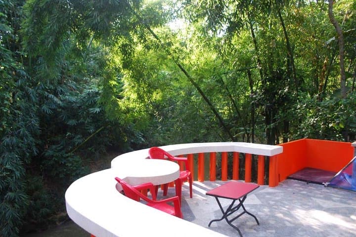 Hermitage Guest House's curved terrace with red chairs overlooking a forest stream
