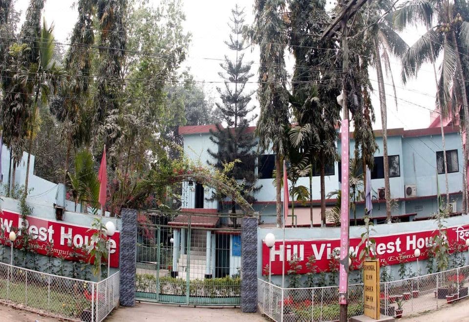 Front gate and exterior of Hill View Rest House with red signage reading the property name, palm trees, and the light-blue two-storey building behind