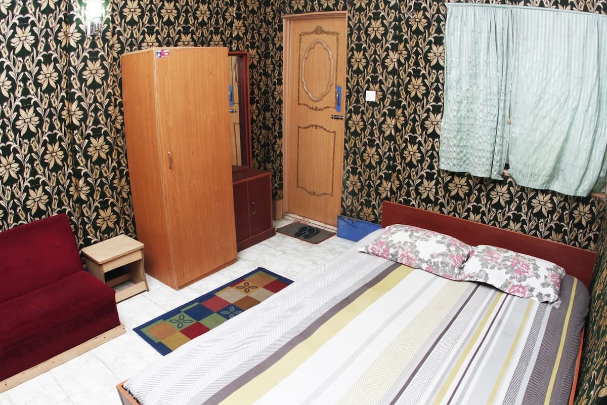 Guest room with dark green floral wallpaper, wooden wardrobe, mirrored dresser, and a striped-bedding double bed