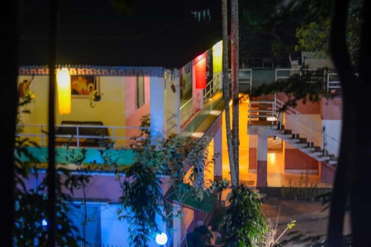 Himachol Resort's colourfully lit building at night, seen through trees, with open-air stairwells and balconies