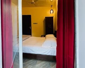 The Pryiotomeshu room at Joldhara Resort, seen through red curtains, with yellow walls and a made-up bed
