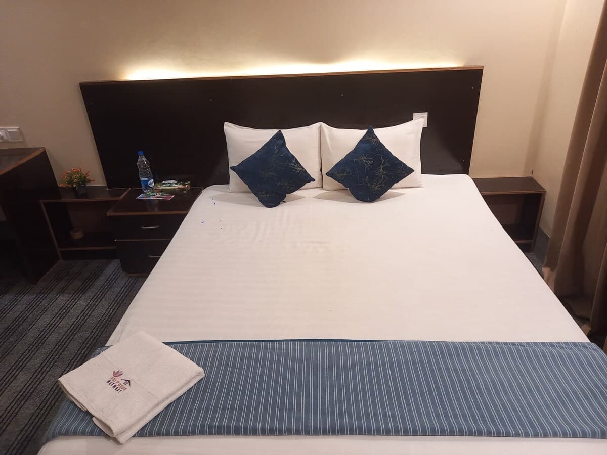 Made-up double bed with navy accent pillows and a folded towel embroidered with the Jolpoddo Retreat lotus logo resting on the foot of the bed