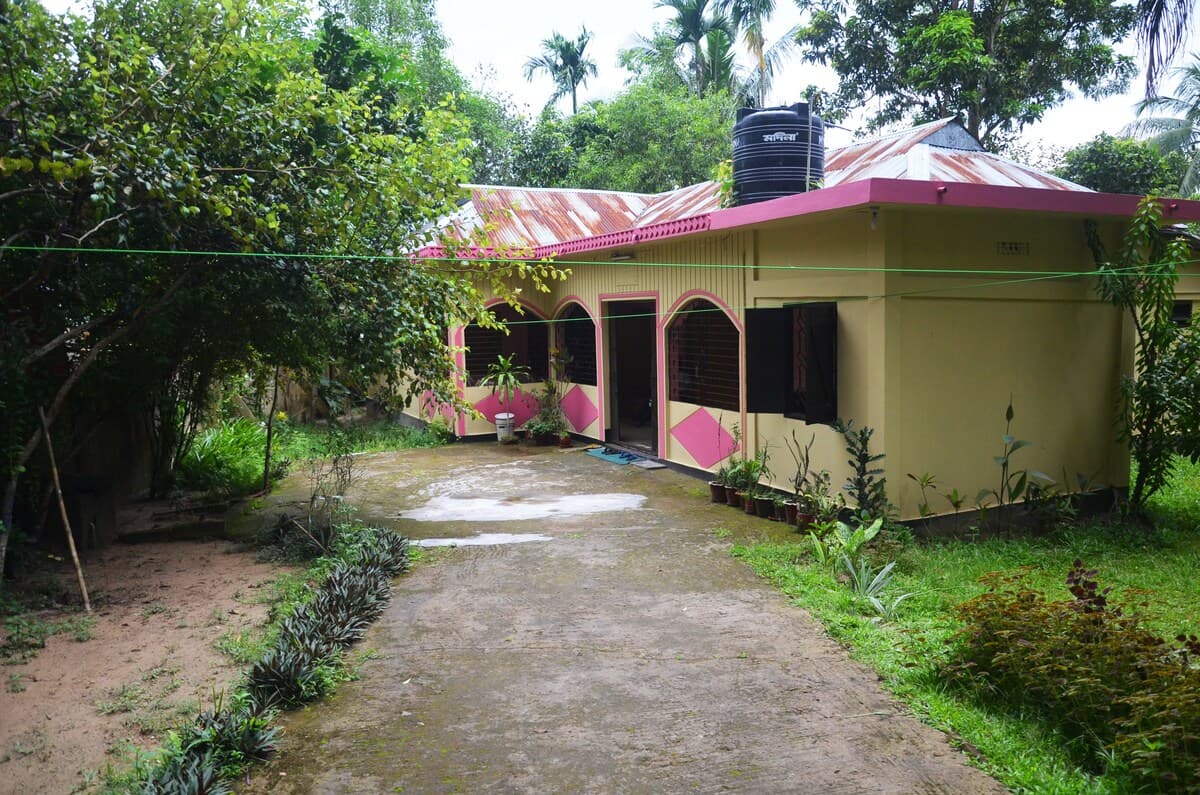 Exterior of the yellow and pink cottage building with tin roof, surrounded by garden and trees