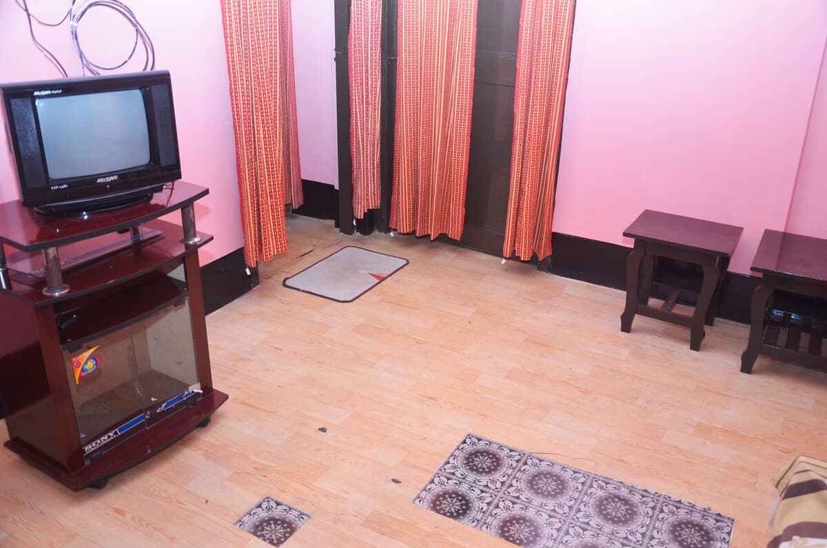 Guest room with a TV on a wooden cabinet, pink walls, and patterned curtains