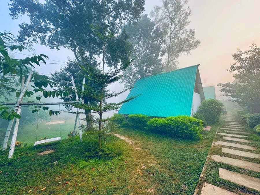 A cottage with a turquoise roof at Nirjon Nature's Hideout wrapped in morning mist