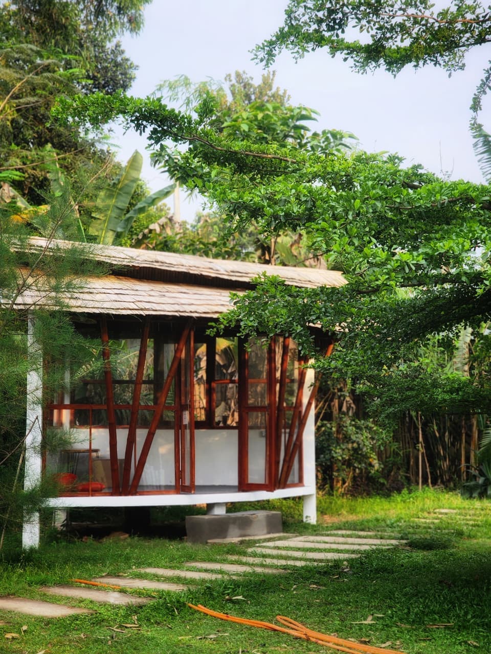 An open-air bamboo-framed pavilion on stilts at Nirjon Nature's Hideout, reached by a stepping-stone path through the garden