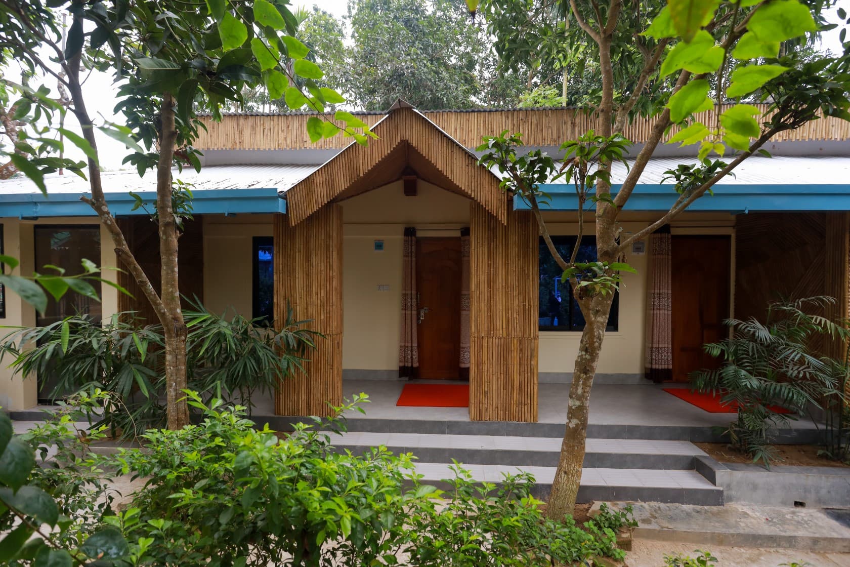 The bamboo-fronted entrance porch of Maasranga Deluxe Room at Nishorgo Eco Cottage, with two red welcome mats