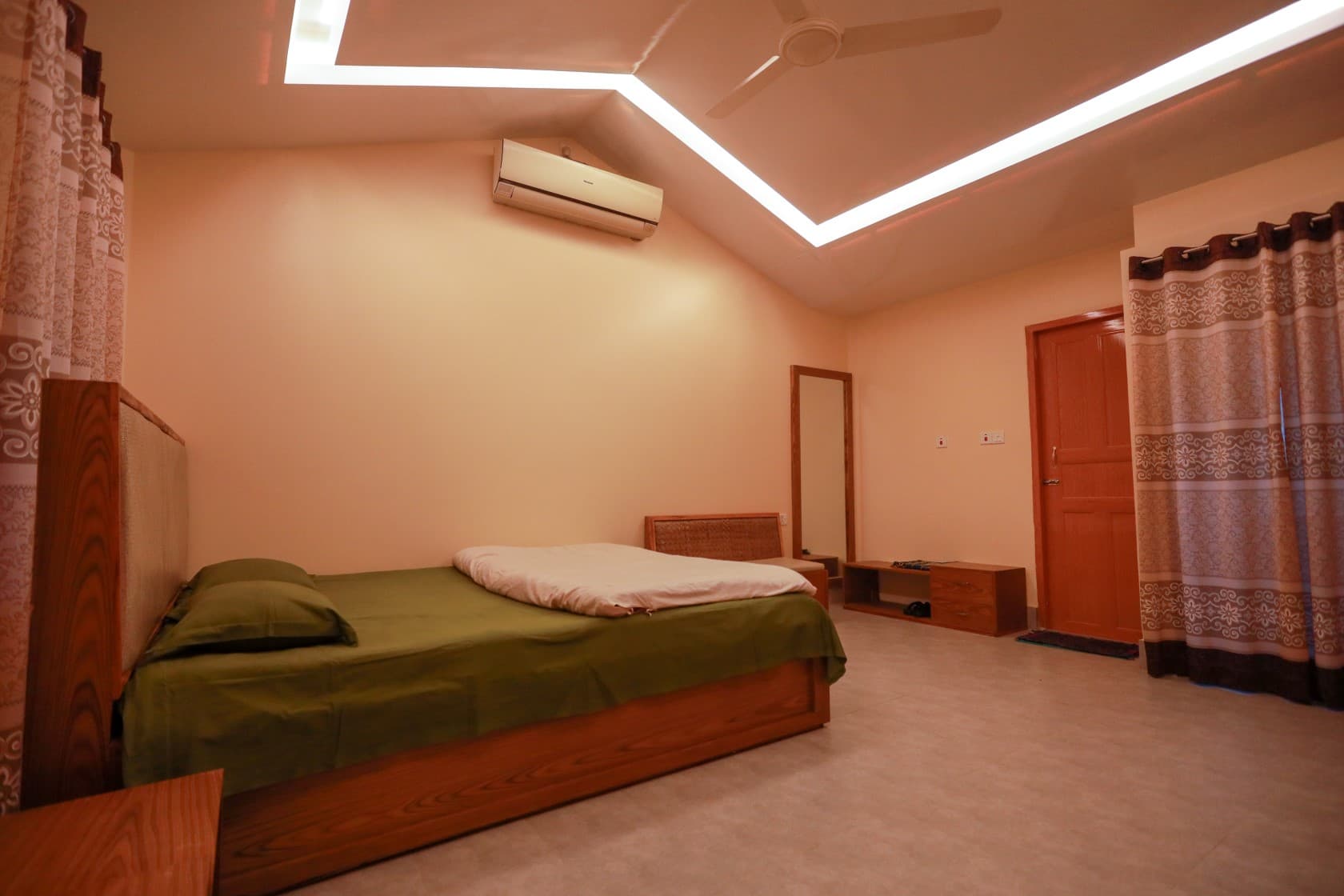 Inside the Maasranga Deluxe Room — a green-covered bed, wall-mounted AC unit and a full-length mirror