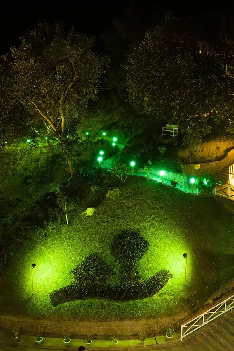 Novem Eco Resort's hillside grounds lit up green at night, with a tree-and-hand topiary cut into the lawn
