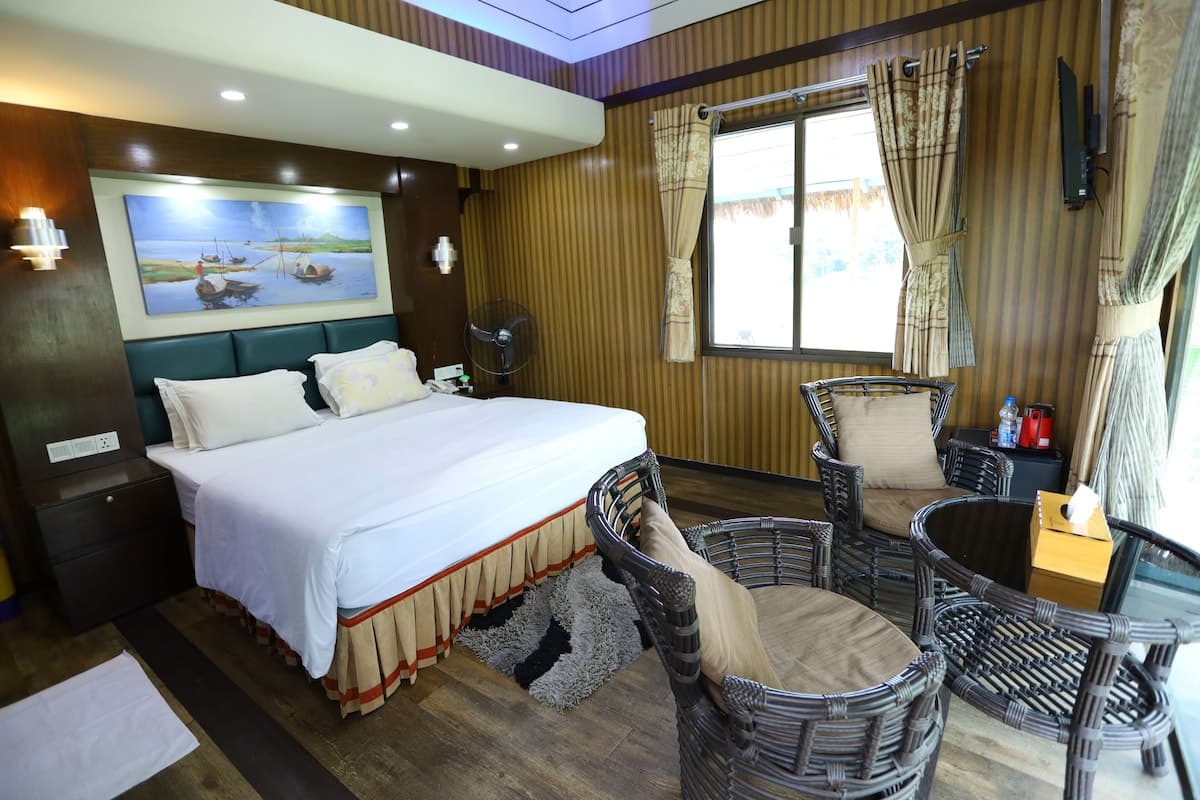 A wood-panelled room at Rangauti Resort with a teal headboard, rattan armchairs, and a lake view through the window