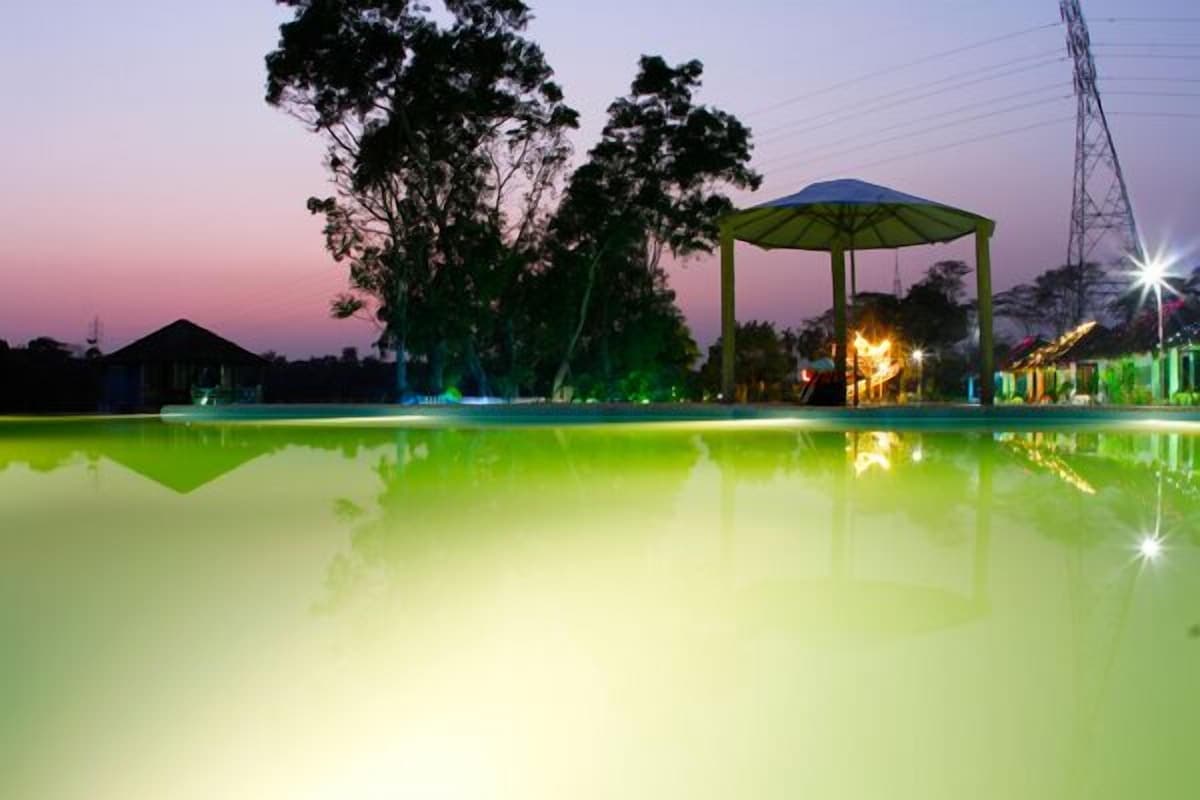 Rangauti Resort's lakeside pool and gazebo lit up at dusk, reflecting a pink-and-green sky