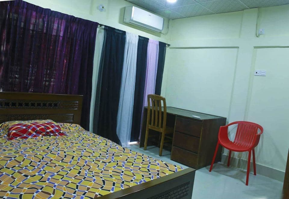 A guest room at Resort World with a patterned bedspread, work desk, and red chair