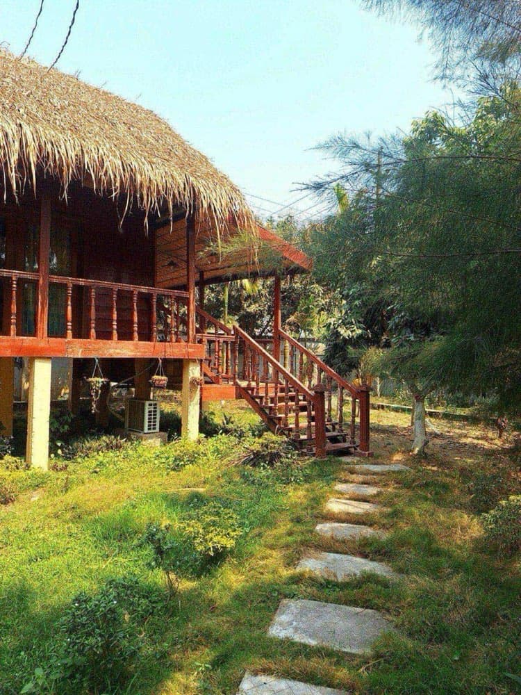 A wooden cottage with a thatched roof at Royal Green Resort surrounded by trees