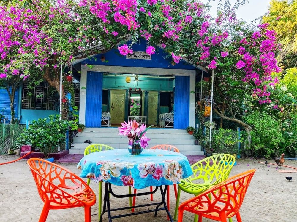 Siddiquibad Homestay's flower-covered blue porch with a Bengali nameboard reading Siddiquibad