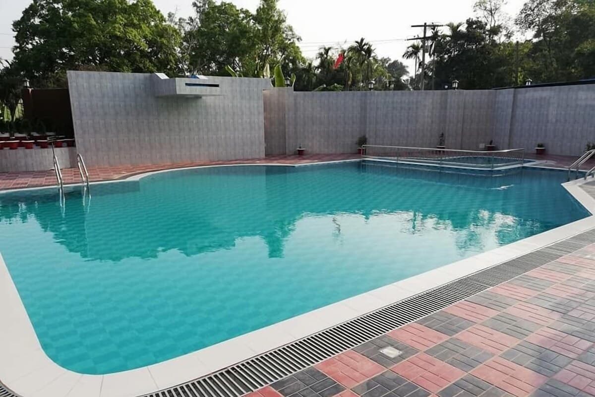 Outdoor swimming pool with tiled red-and-grey deck, steps and handrails into the water, surrounded by a stone wall and trees