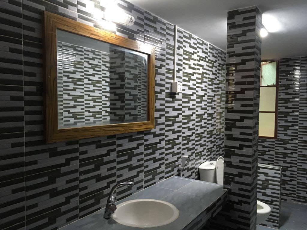 Bathroom finished in staggered grey and black mosaic tile, with a timber-framed mirror above a stone counter and basin, and a toilet beyond a tiled partition