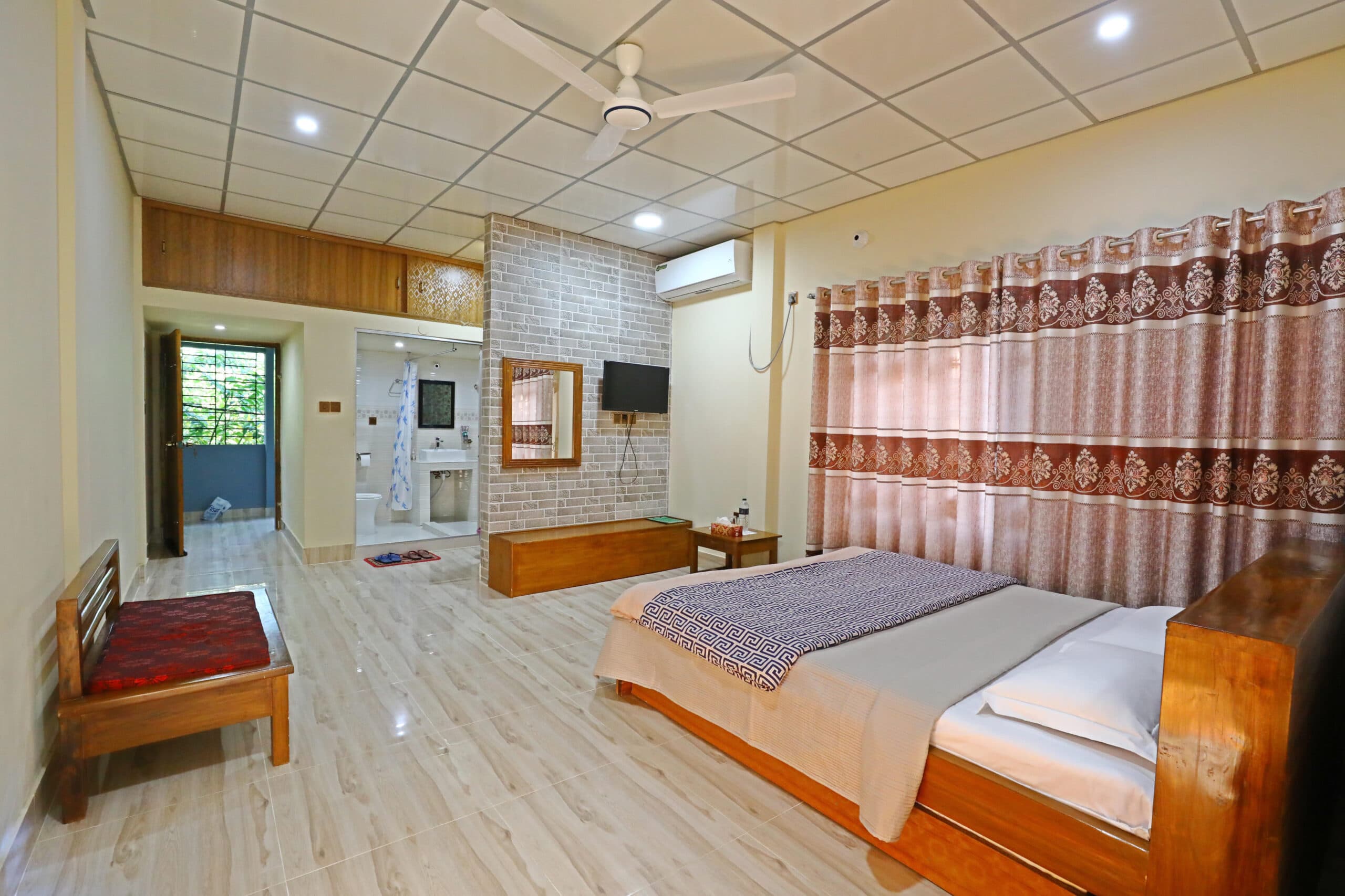 A spacious room at Swiss Valley Resort with a wooden bed, patterned curtains, a wall-mounted TV, and an open-plan bathroom