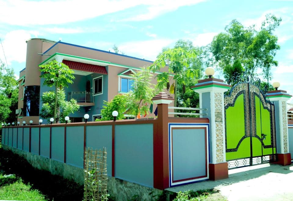 Full exterior of Tamim Resort, a two-storey building with a rounded corner tower behind a boundary wall and green entrance gate