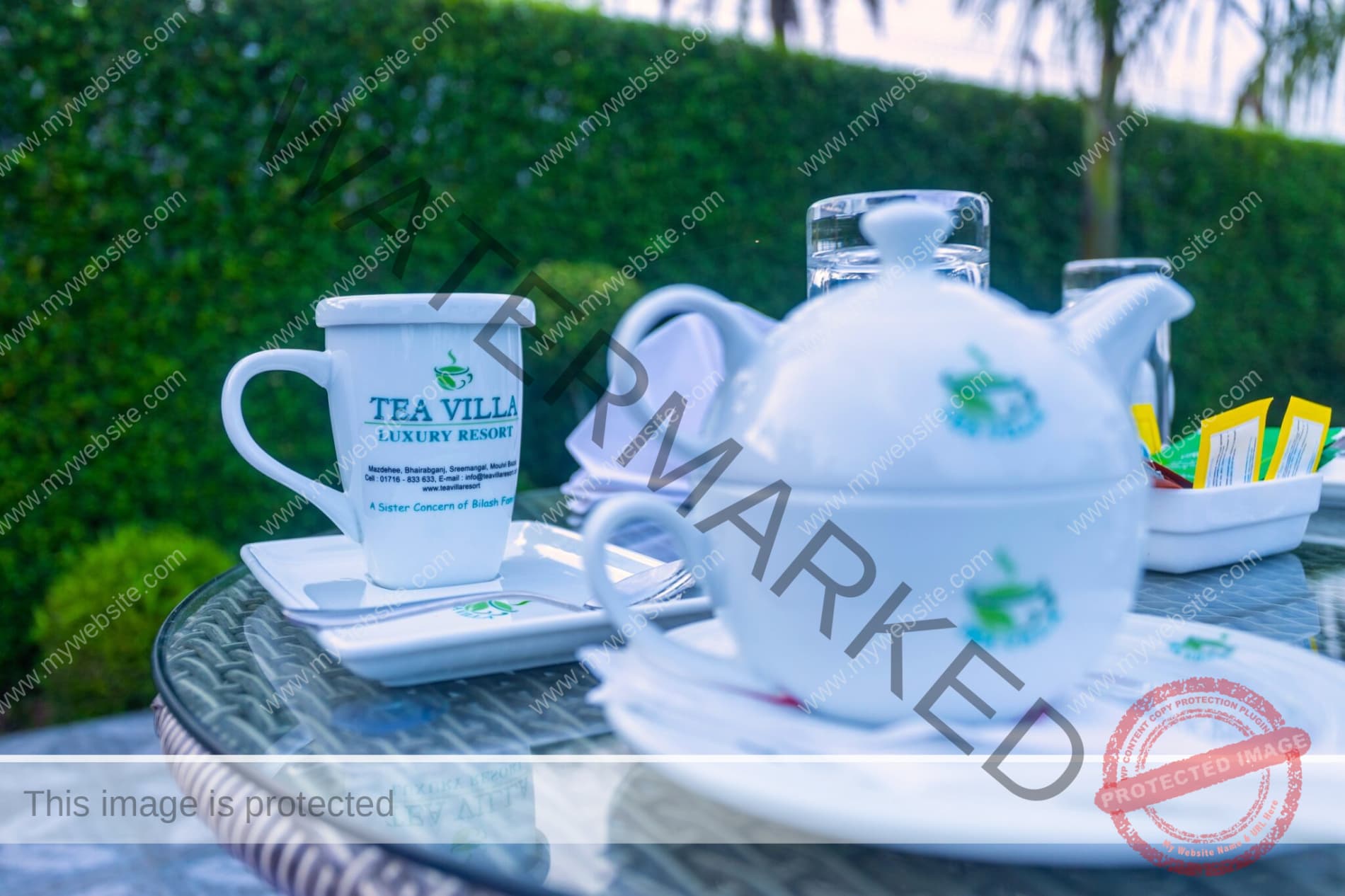 A branded Tea Villa Luxury Resort mug and teapot printed with the property's address and phone number, set on an outdoor table