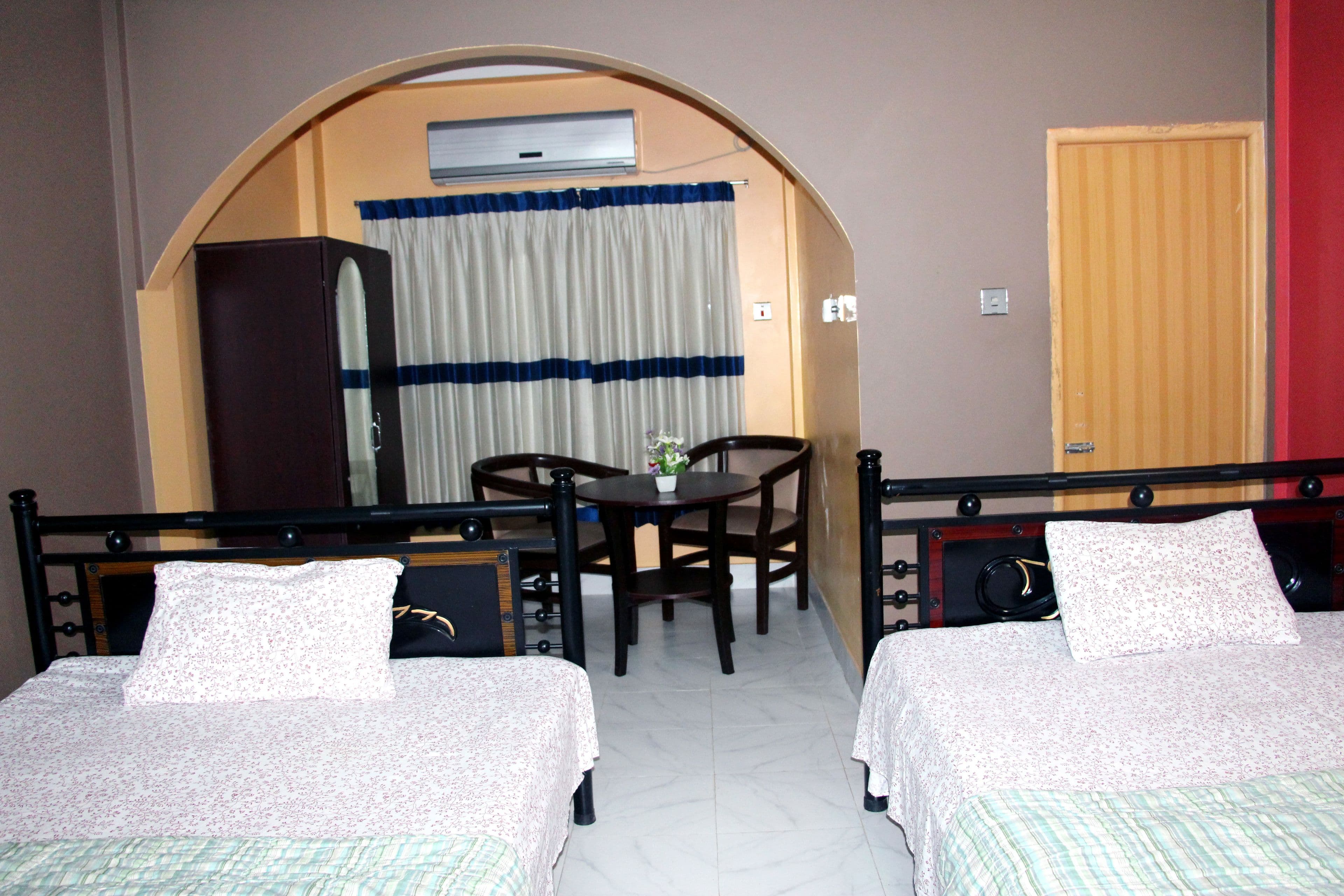 Twin-bed guest room with dark wood headboards, an arched doorway to a curtained sitting nook with a round table and two chairs