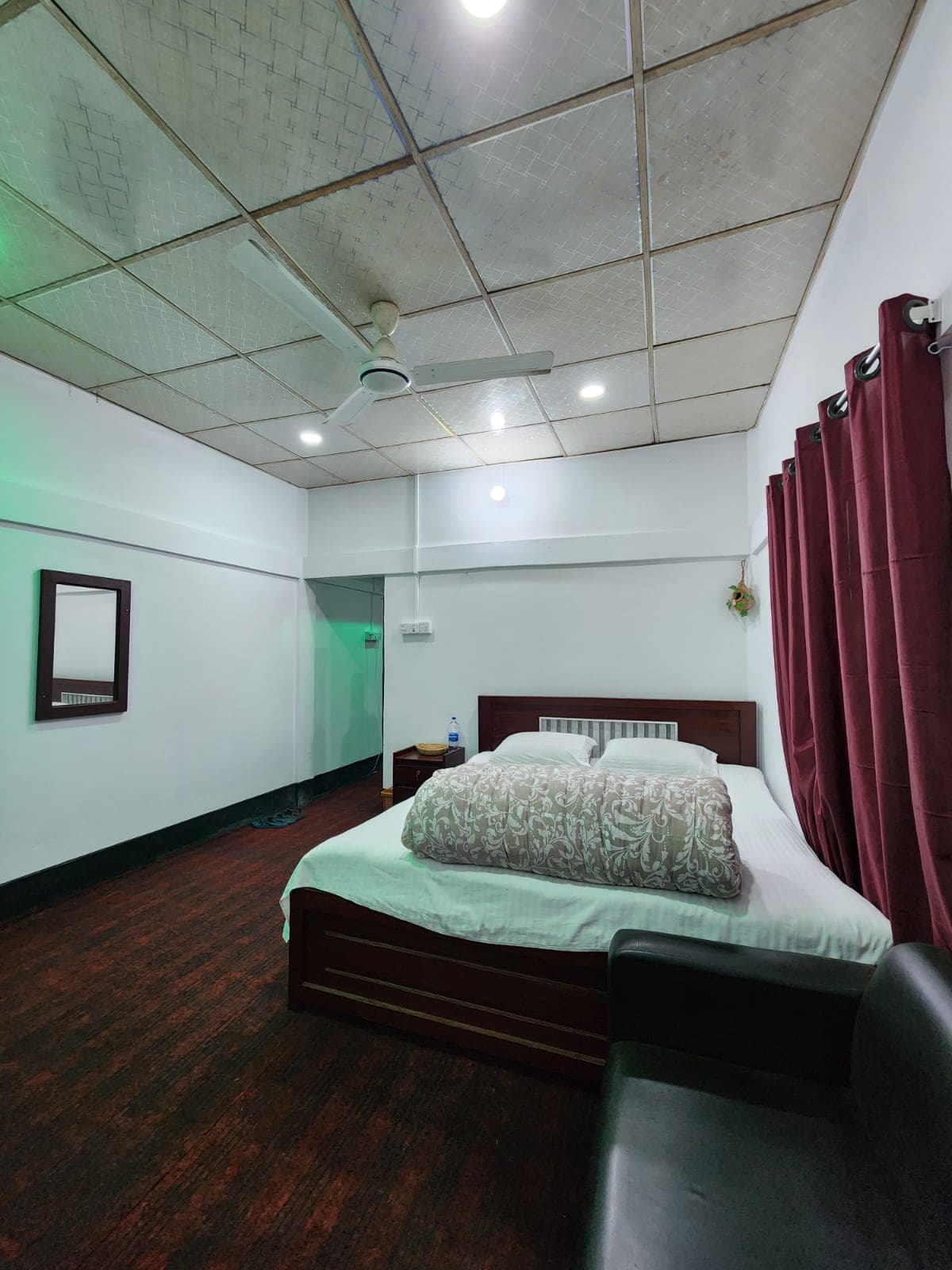 Guest room with a wall mirror, maroon curtain, and a plain white-bedded double bed