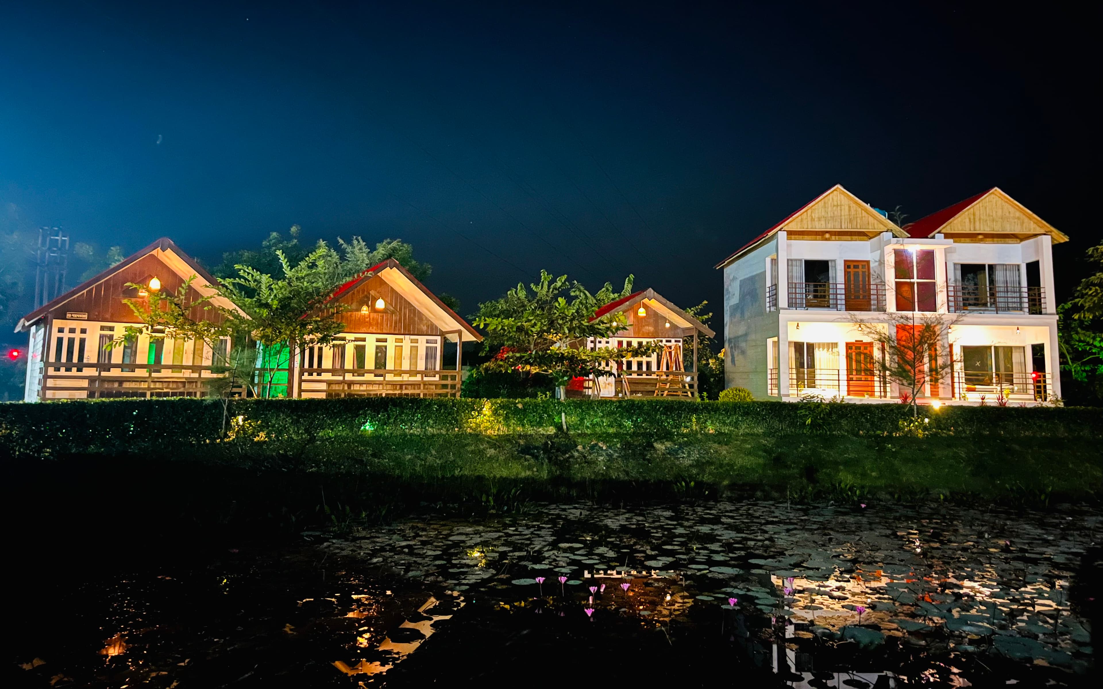 Waterlily Resort's cottages and two-storey building lit up at night, reflected in the lily pond in front