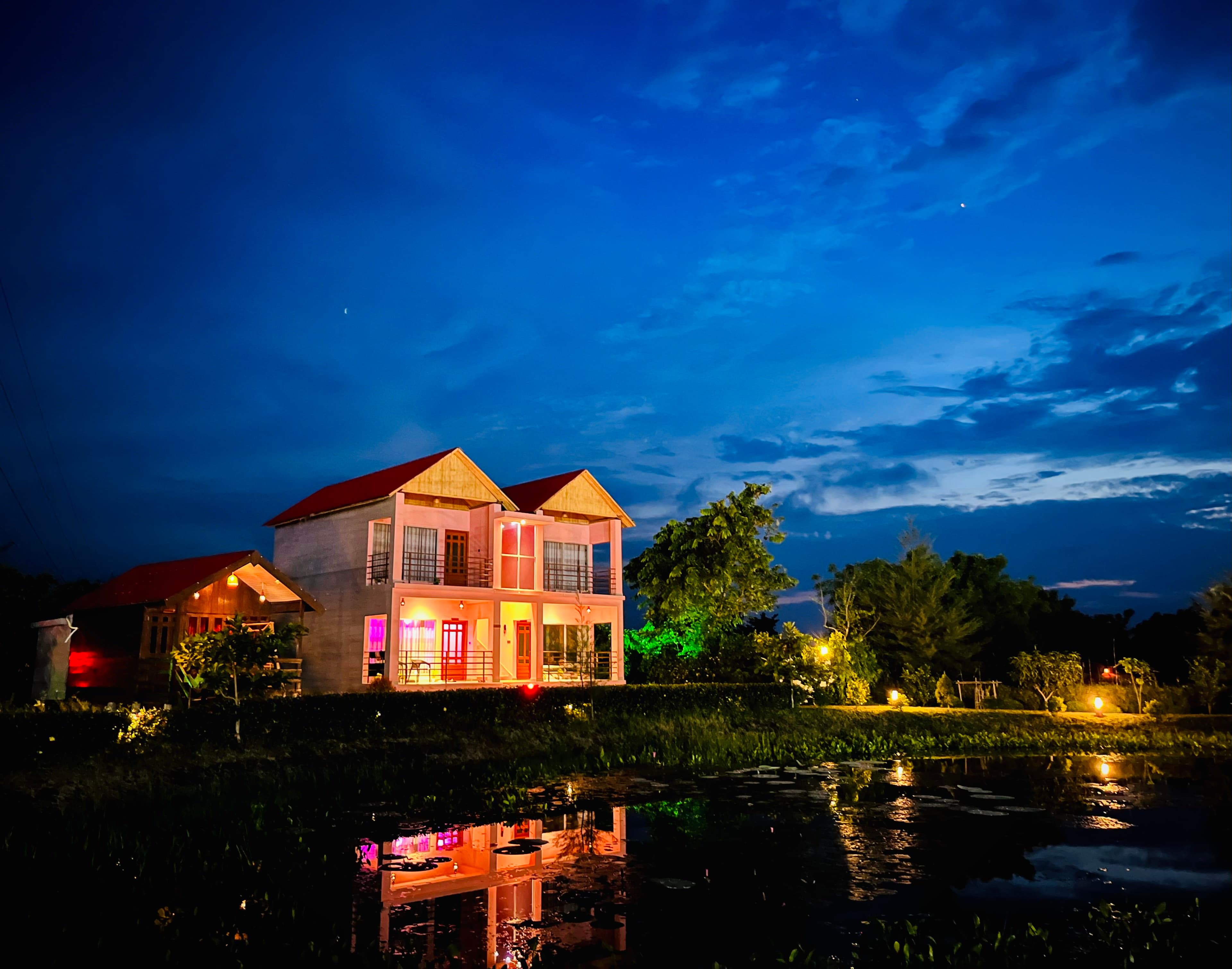 Dusk exterior of the resort's main two-storey building beside the water lily pond, lights on