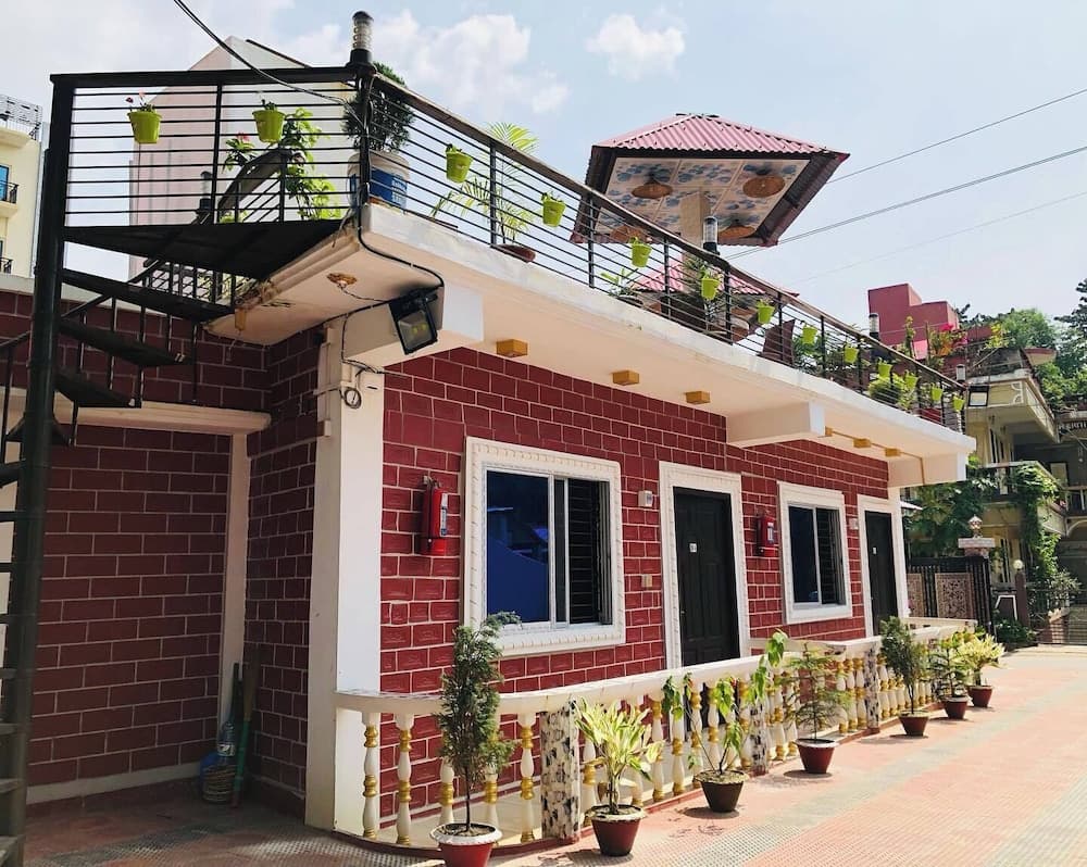 Daytime exterior of the red-brick building with a rooftop terrace, hanging planters, and spiral staircase