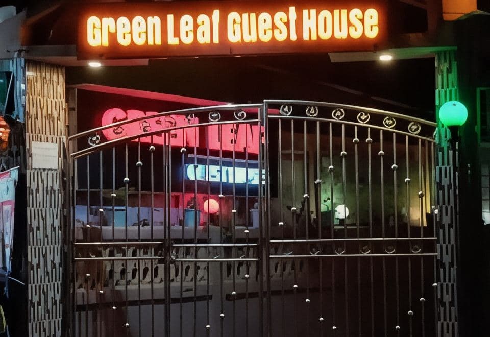 Green Leaf Guest House's entrance gate at night, lit by its neon signage over the front desk