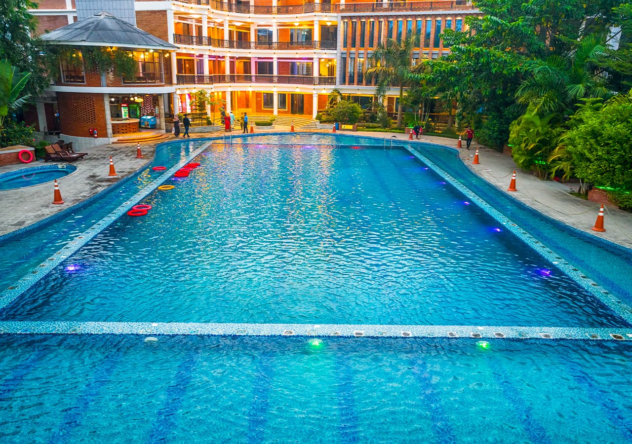 Lemon Garden's long lit swimming pool at dusk with floating rings, sun loungers and the resort building behind