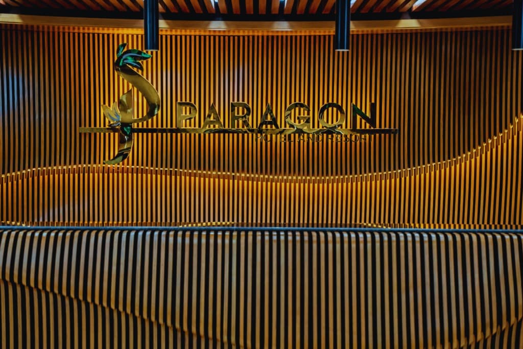 Paragon Hotel & Resort's illuminated reception desk with the gold Paragon logo mounted on a slatted wood wall