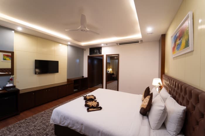 A Deluxe King room at Paragon with a tufted brown headboard, wall-mounted TV and an ensuite doorway