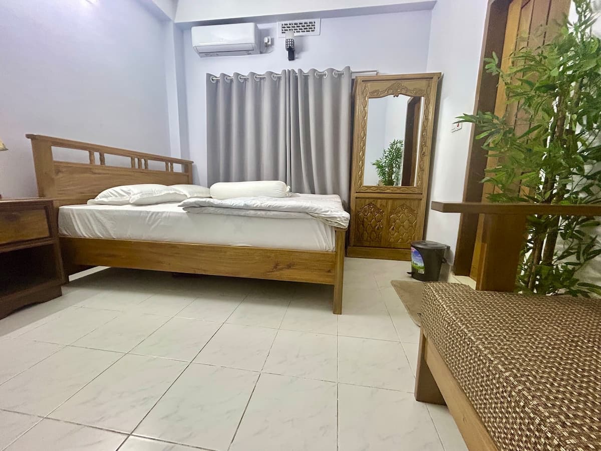 Wooden double bed with air conditioning, mirror, and tiled floor in the private room near Sreemangal railway station
