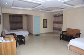 A twin-bed room at Sreemangal Inn with a coffered ceiling, sofa, and armchair