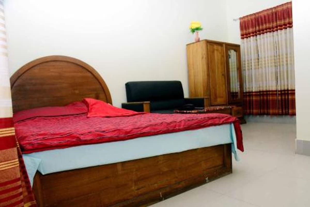 Guest room with a dark-wood double bed and red bedspread, black leather sofa, and a mirrored wardrobe against a striped curtain
