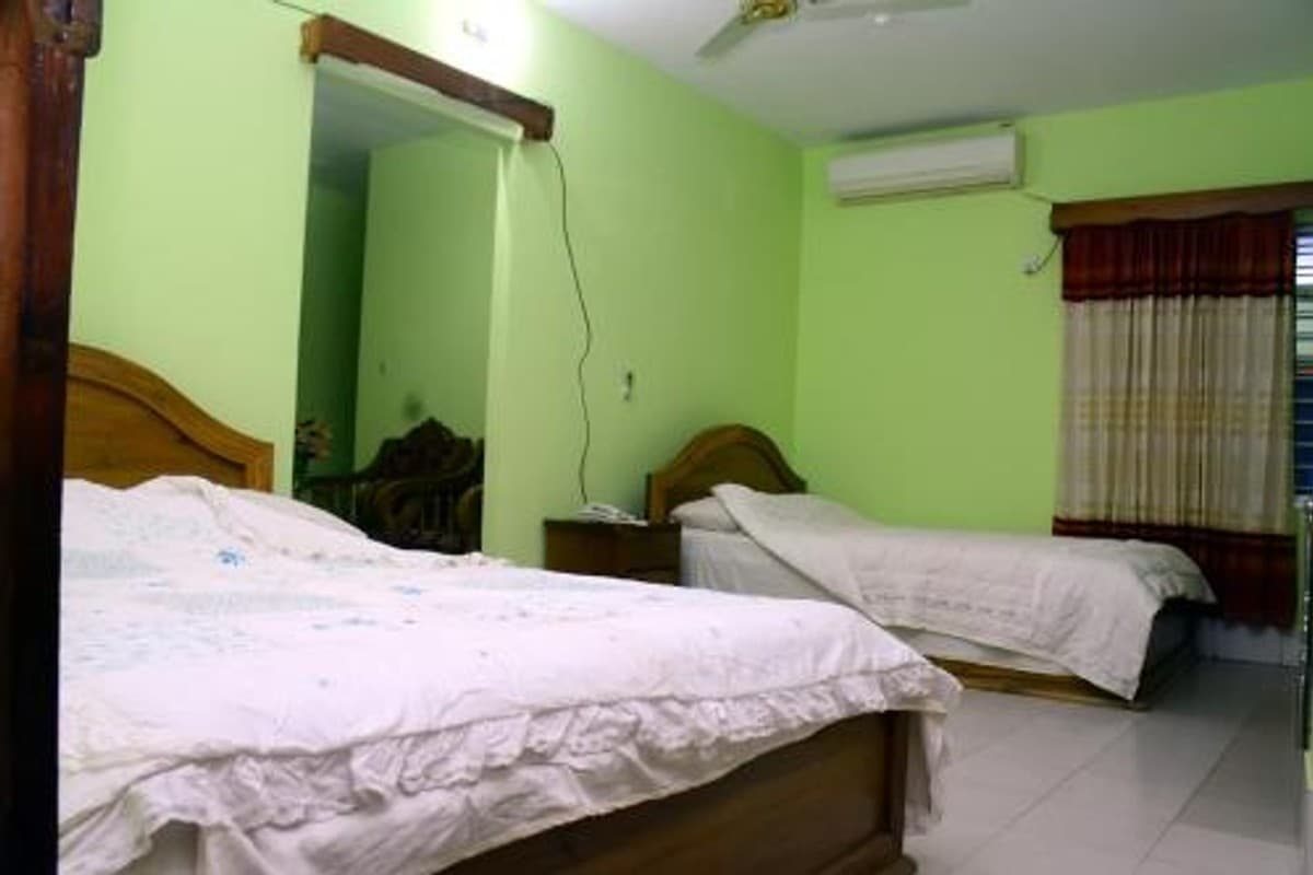 Green-walled twin room with wooden bed frames, a wall-mounted air conditioner, and striped maroon-and-cream curtains