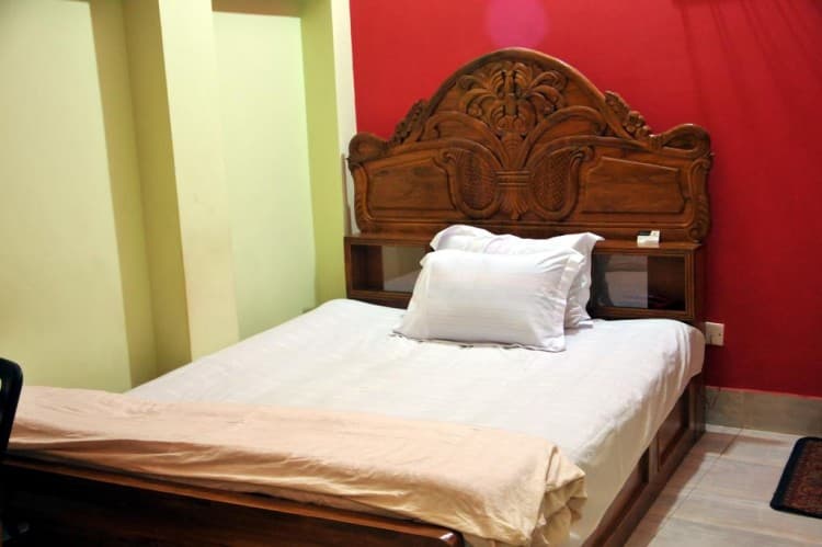 Double bed with a carved wooden headboard, white bedding, and a red accent wall in a guest room